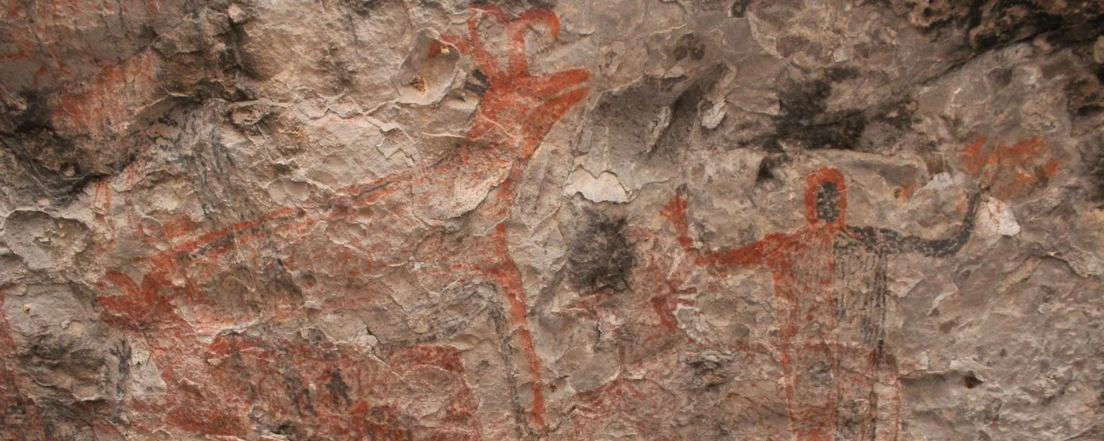 Pintura rupestre en el techo de la cueva El Ratón: figuras de venados en rojo y una figura humana de brazos abiertos sobre la roca clara