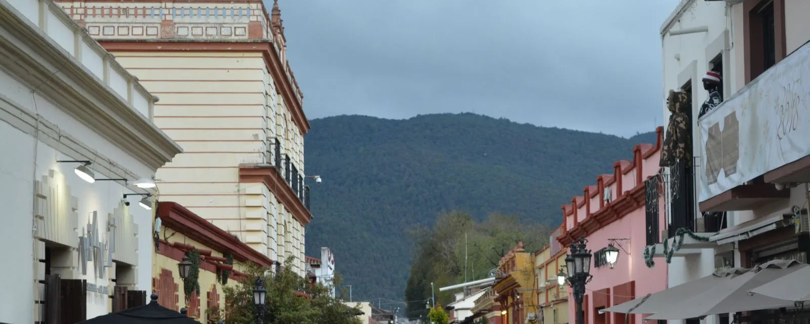 Una calle de San Cristóbal de las Casas entre fachadas de colores con balcones de herrería, cerrada al fondo por el cerro boscoso
