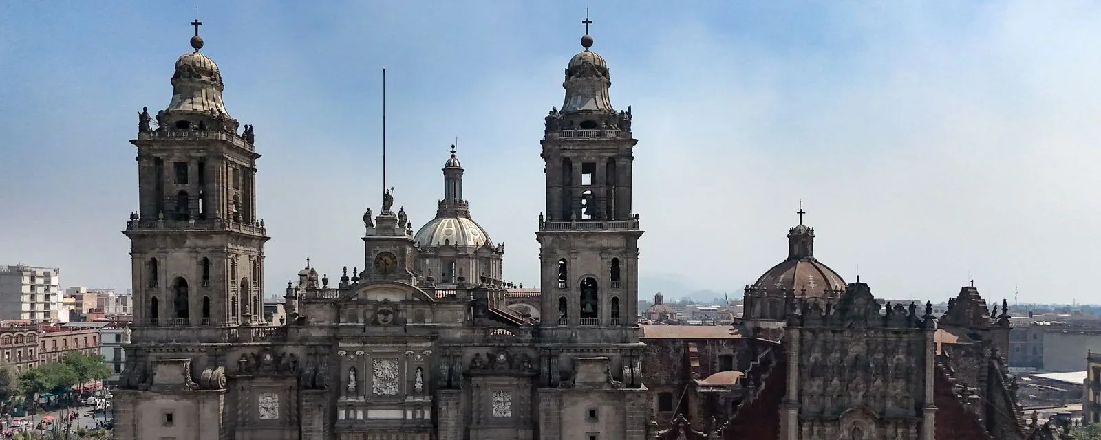 Las dos torres y la cúpula de la Catedral Metropolitana vistas desde arriba, con las azoteas del Centro Histórico y los cerros del valle al fondo