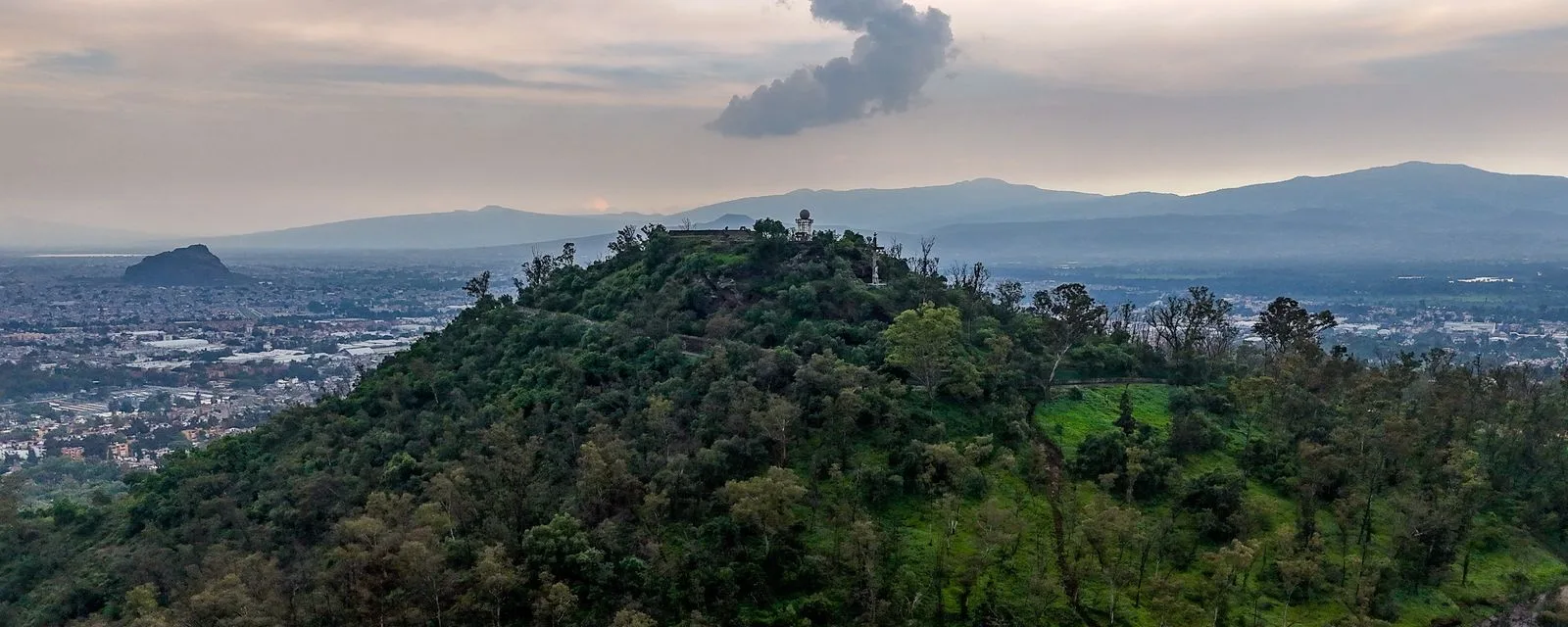 El Cerro de la Estrella desde el aire: la ladera arbolada con la construcción de la cima, y la mancha urbana de Iztapalapa extendiéndose alrededor