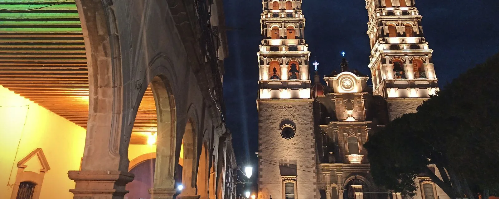 Las dos torres iluminadas de un templo de Salvatierra vistas de noche desde los portales, con los arcos de cantera en primer plano