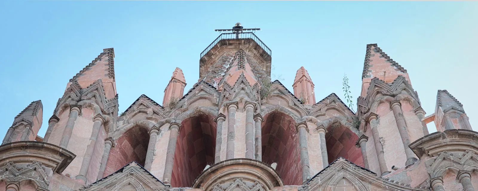 Las agujas neogóticas de cantera rosa de la Parroquia de San Miguel Arcángel vistas desde el pie de la fachada, recortadas contra el cielo