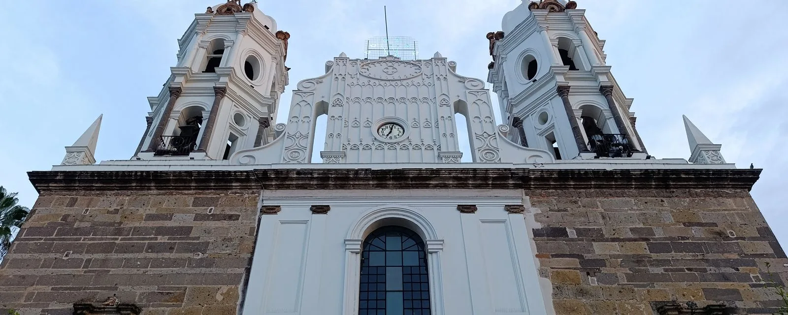 La parroquia de Nuestra Señora de la Soledad en Tlaquepaque vista desde el pie: su remate blanco labrado con reloj, entre dos campanarios, sobre el muro de cantera