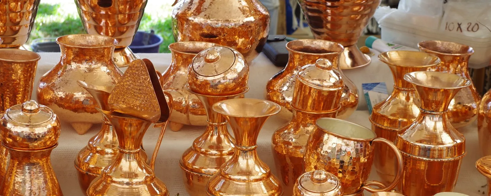 Piezas de cobre martillado de Santa Clara del Cobre puestas en venta: jarras, copas y ollas brillando bajo la luz del mercado