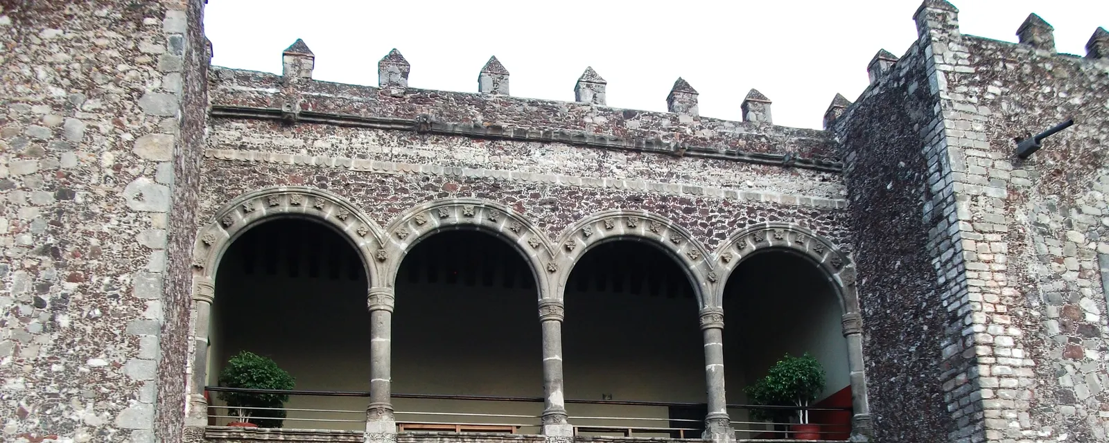 La logia del Palacio de Cortés en Cuernavaca: cuatro arcos de piedra sobre columnas, coronados por almenas, en el muro de mampostería del edificio