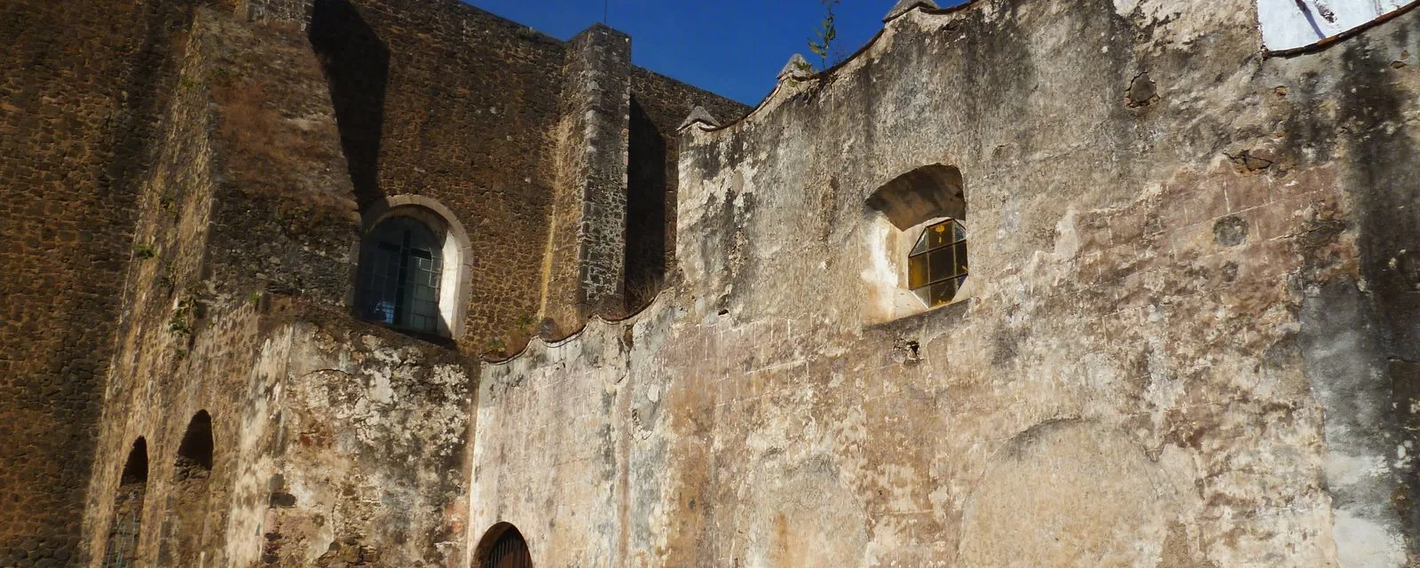 El muro exterior del ex convento de San Juan Bautista en Tlayacapan: mampostería descarnada por los siglos, con contrafuertes y dos ventanas de arco