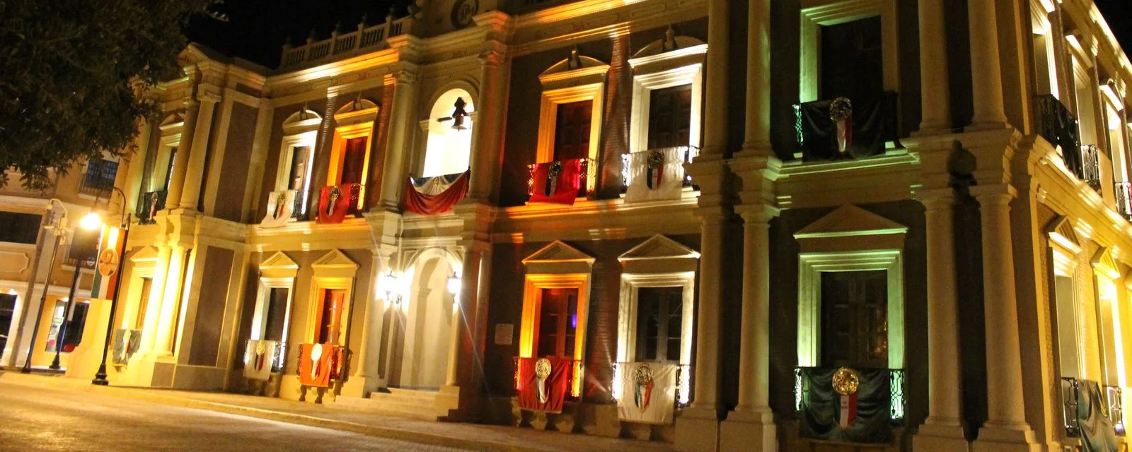 El palacio municipal de Linares iluminado de noche durante las fiestas patrias, con los balcones vestidos de tricolor