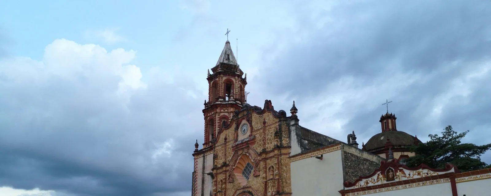 La misión de Jalpan de Serra bajo un cielo de tormenta: su portada de argamasa labrada y la torre de cantera rojiza sobre el muro encalado