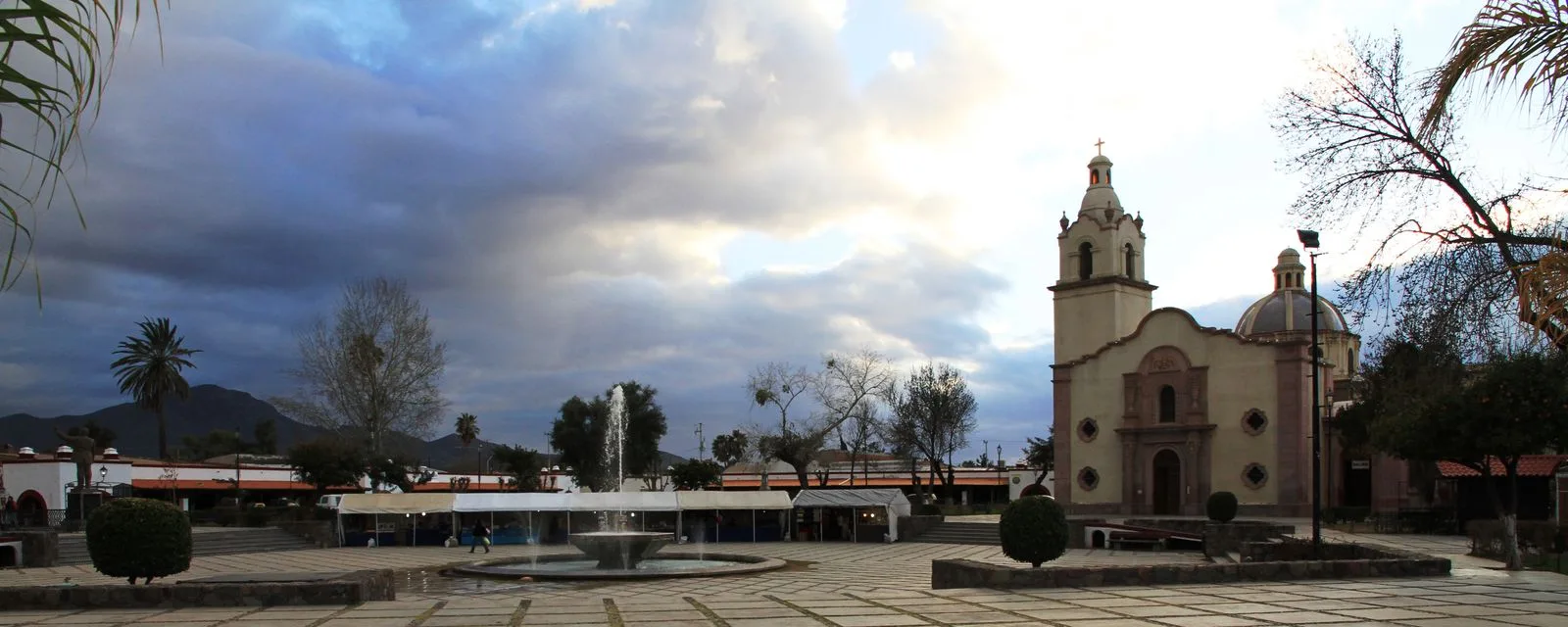 La plaza de Magdalena de Kino al atardecer: la fuente al centro, el templo a la derecha y la cúpula del mausoleo del padre Kino junto a él