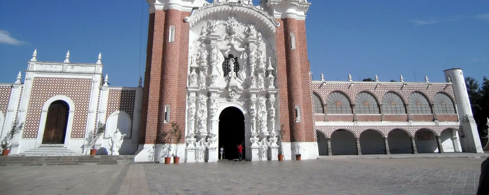 La fachada del Santuario de Ocotlán en Tlaxcala: el frontispicio de argamasa blanca labrada entre dos torres de ladrillo rojo con azulejo
