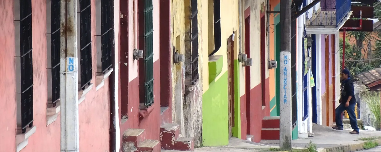 Una calle en cuesta de Coatepec: la hilera de fachadas pintadas de rosa, amarillo y verde con sus ventanas enrejadas